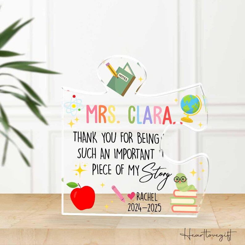 May include: A clear acrylic puzzle piece with the text "MRS. CLARA. THANK YOU FOR BEING SUCH AN IMPORTANT PIECE OF MY Story RACHEL 2024-2025". The design includes a red apple, a pencil, a globe, a worm with glasses, and books.