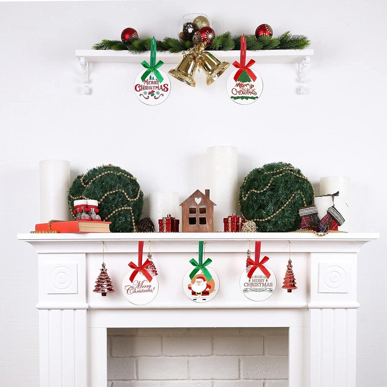 May include: A white mantelpiece decorated for Christmas with ornaments, candles, and greenery. Round ornaments with "Merry Christmas" text and a Santa Claus image hang from the mantel. A shelf above holds bells and more decorations.