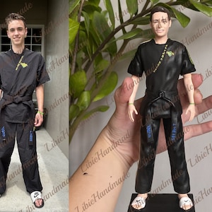 May include: A black and white custom figurine of a person wearing a black martial arts uniform with a black belt. The figurine is standing on a black base.