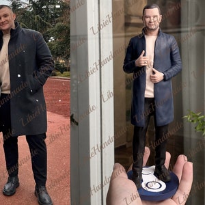 May include: A hand-painted figurine of a person wearing a blue coat, black trousers, and a light pink shirt. The figurine is standing on a blue and white circular base.