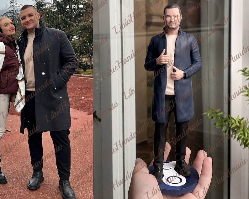 May include: A hand-painted figurine of a person wearing a blue coat, black trousers, and a light pink shirt. The figurine is standing on a blue and white circular base.