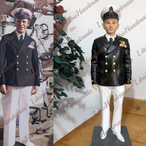 May include: A black and white figurine of a person wearing a navy blue double-breasted jacket with gold buttons, white pants, and a black and white hat. The figurine is standing on a black base.