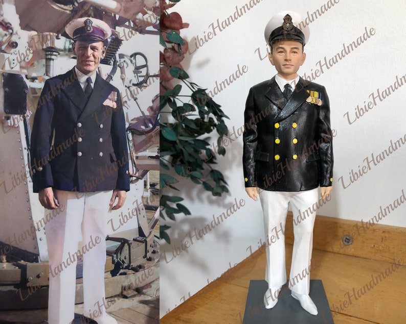May include: A black and white figurine of a person wearing a navy blue double-breasted jacket with gold buttons, white pants, and a black and white hat. The figurine is standing on a black base.