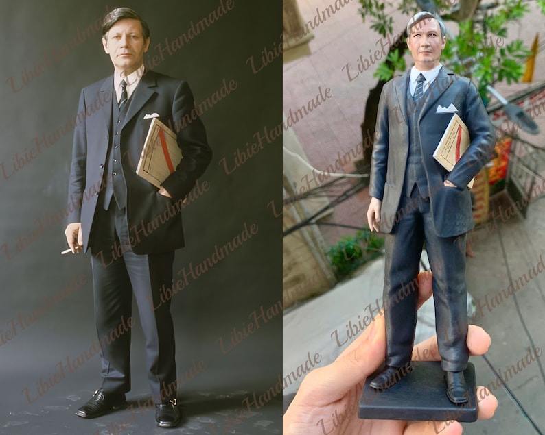May include: A black and white figurine of a man wearing a suit and holding a folder. The figurine is standing on a black base.