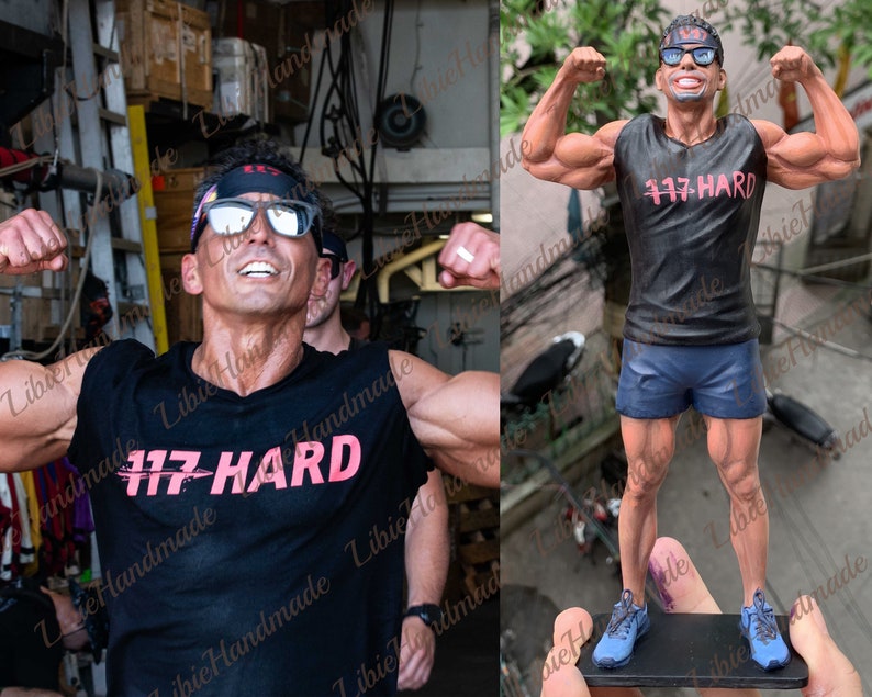 Puede incluir: Una camiseta negra sin mangas con el texto "117 HARD" impreso en rosa. La camiseta la lleva puesta una figura de un hombre musculoso con una cinta negra para la cabeza y gafas de sol. La figura est&aacute; de pie sobre una base negra.
