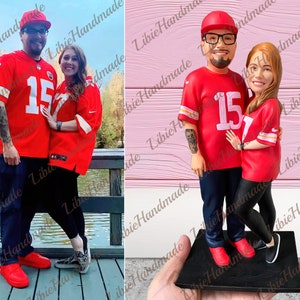 Può includere: Una statuetta personalizzata di una coppia che indossa maglie rosse con il numero 15. La statuetta è in piedi su una base nera.