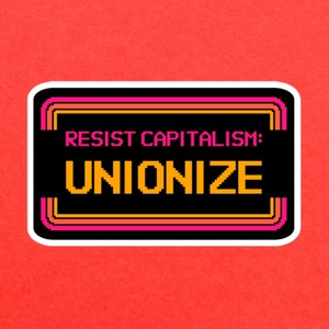 May include: A black and white sticker with a pink and orange border. The sticker says "Resist Capitalism: Unionize" in a pixelated font.