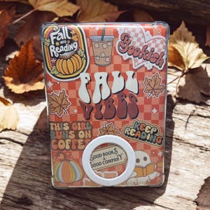 Könnte beinhalten: Eine transparente Handyhülle mit einem Herbst-Design. Die Hülle zeigt die Worte "Fall Vibes" und andere herbstbezogene Grafiken, darunter Kürbisse, Blätter und den Text "This girl runs on coffee". Ein weißer Handyhalter ist angebracht.