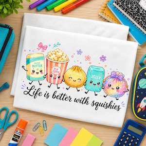 May include: A white fabric surface featuring a colorful graphic of five smiling, anthropomorphic food items including a butter stick, popcorn, a dumpling, jelly, and a round treat, with the text "Life is better with squishies" printed below.