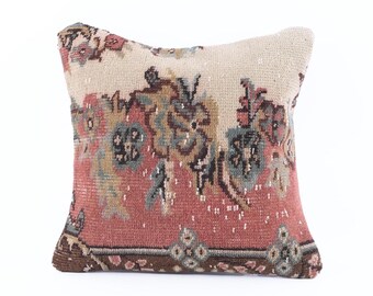 May include: Square cushion with a vintage rug design. The cushion has a cream-coloured centre with a floral pattern in shades of red, blue, and brown. The bottom border is a darker brown.