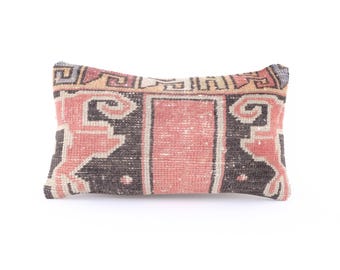 May include: A rectangular pillow with a pink, black, and white geometric pattern. The pillow is made of woven fabric and has a fringed edge.