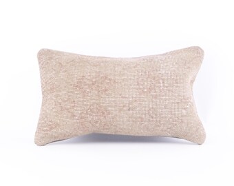 May include: A rectangular beige pillow with a woven texture and faded pink patterns. The pillow is a decorative item, likely for a sofa or bed, and is set against a white background.