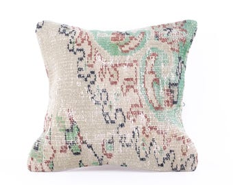 May include: A beige throw pillow with a colorful floral pattern in shades of green, red, and black. The pillow is made from a soft, woven fabric and has a subtle distressed look.