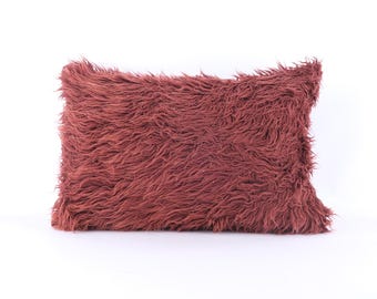 May include: A soft, plush pillow with a burgundy faux fur cover. The pillow is rectangular and has a fluffy texture.