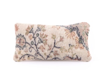 May include: A rectangular throw pillow with a floral pattern in shades of beige, brown, and green. The pillow has a white background and a subtle sheen.