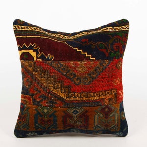 May include: A square pillow with a patchwork design featuring different colored and patterned fabrics. The pillow is made of a dark blue, red, and gold fabric with intricate geometric patterns.