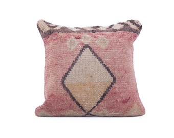 May include: Square decorative pillow with a pink and beige geometric design. The pillow features a diamond pattern in the center and a textured, woven appearance. The edges have a darker, patterned border.