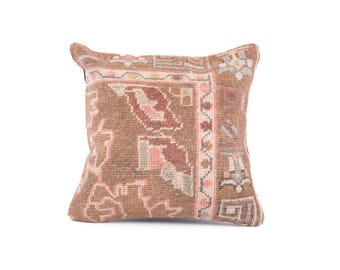 May include: Square decorative pillow with a woven, textured design. The pillow features a brown and tan color palette with accents of pink and light green. The pattern includes geometric and floral elements, creating a vintage or bohemian aesthetic.