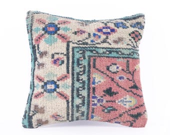 May include: A square cushion with a floral pattern in shades of pink, blue, and green. The cushion is made from a woven fabric with a distressed look.