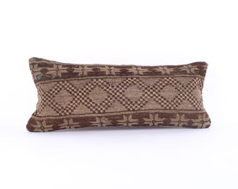 May include: Rectangular decorative pillow with a woven design. The pillow features a repeating pattern of diamonds and geometric shapes in shades of brown and tan. The pillow is designed for home decor.