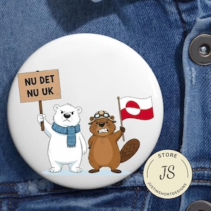 Puede incluir: Un botón blanco con un oso polar y un castor de dibujos animados. El oso polar sostiene un cartel que dice "NU DET NU UK", mientras que el castor sostiene una bandera roja y blanca. Un pequeño logotipo de la tienda está en la esquina inferior derecha.