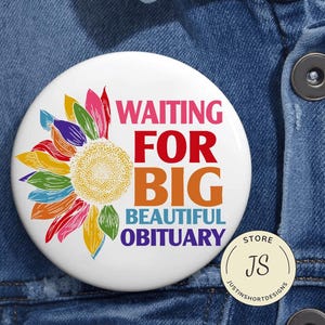 以下が含まれることがあります： ピンク、赤、オレンジ、青で「WAITING FOR BIG BEAUTIFUL OBITUARY」と書かれた白いバッジ。左側にはカラフルなヒマワリのデザインがあります。小さな丸いストアロゴが右下にあります。