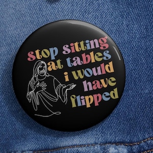 May include: A black button with a white outline of Jesus with the text "Stop sitting at tables I would have flipped" in rainbow colors.