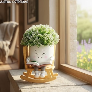 以下が含まれることがあります： 微笑む顔の形をした、気まぐれな白い植木鉢。ミニチュアのロッキングチェアに座り、本を持っています。植木鉢には緑と白の人工葉が詰められています。魅力的な装飾品です。