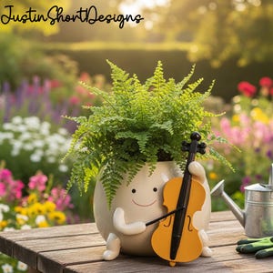 May include: A quirky, cream ceramic plant pot in the shape of a character, holding a yellow violin. The pot is filled with lush green ferns. The text "Justin Short Designs" is visible. The background is a blurred garden scene with various colorful flowers.