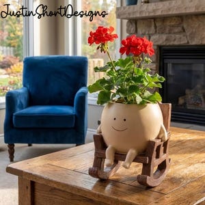 May include: A whimsical beige planter shaped like a smiling egg, seated in a wooden rocking chair, holding a vibrant red geranium. The planter has arms and legs. The text "Justin Short Designs" is in the upper left corner.