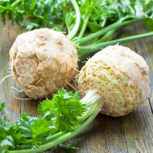 May include: Two fresh celeriac root vegetables with green celery stalks and leaves. The celeriac has a rough, beige exterior and is displayed on a rustic wooden surface. The image highlights the natural textures and colors of the produce.