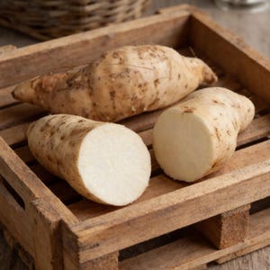 May include: Three jicama roots, two whole and one cut open, rest in a rustic wooden crate. The jicama has a light brown skin with a rough texture, and the cut reveals a crisp, white interior. The crate is made of weathered wood.