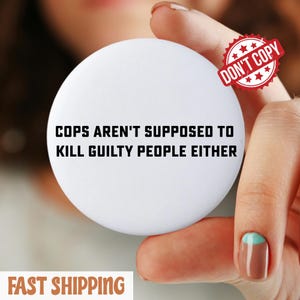 May include: A white, circular badge with the black text "COPS AREN'T SUPPOSED TO KILL GUILTY PEOPLE EITHER". A red "DON'T COPY" stamp is visible. The badge is held by a person.