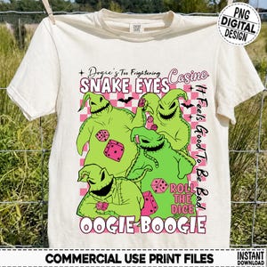 May include: A cream-colored t-shirt featuring a graphic print of three lime green Oogie Boogie characters from The Nightmare Before Christmas, pink dice, and a pink checkered background with the text Oogie's Too Frightening Casino Snake Eyes.