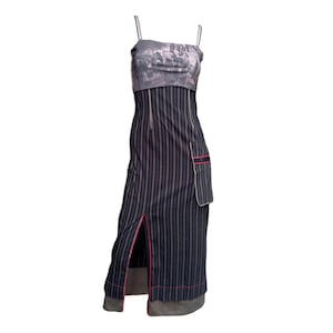 May include: A sleeveless, floor-length dress with a unique design. The top is a gray and white pattern, while the lower portion features black pinstripes with pink trim. A side pocket and a slit add detail to the dress.