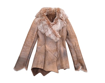Peut inclure: Veste en peau de mouton marron avec un col en fausse fourrure. La veste a une coupe portefeuille avec un ourlet asymétrique. Les manches sont longues et la veste semble être faite d'une matière douce et texturée. Les mesures de la veste ne sont pas visibles.