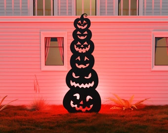 May include: A black metal silhouette of a stack of six jack-o'-lantern pumpkins with different facial expressions. The silhouette is standing in front of a white house with red lighting.