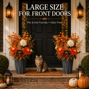 May include: Two dark gray geometric planters filled with orange and white autumn flowers, including dahlias and foliage. The text reads LARGE SIZE FOR FRONT DOORS, Pet & Kid Friendly, Odor-Free. A cat sits on a mat between the two planters.