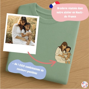 Peut inclure: Sweat-shirt vert sauge avec une photo et une illustration d'une mère et d'un enfant. Le sweat-shirt porte également le texte "+ de 1 000 combinaisons de couleurs possibles" et "Broderie réalisée dans notre atelier en Hauts-de-France."