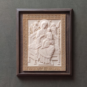 May include: A carved wooden icon depicting the Virgin Mary and baby Jesus. The icon is framed in a dark wood frame with a gold-colored border. The inscription at the bottom reads "Образъ Прст Бдщ Всецарица".