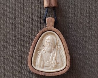 May include: A wooden pendant with a carved image of a bearded man holding a staff. The pendant is on a black cord and has a light brown finish.