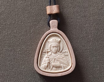 May include: A wooden pendant with a carved image of a woman wearing a crown and holding a cross. The pendant is on a black cord.