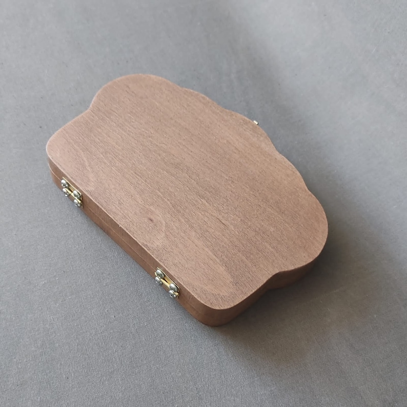 Puede incluir: Una caja de madera con una tapa en forma de nube y dos bisagras de lat&oacute;n. La caja est&aacute; cerrada y la tapa est&aacute; mirando hacia arriba.