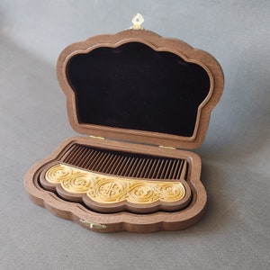 Puede incluir: Un peine de madera con tallas intrincadas en una caja de madera decorativa con forro de terciopelo. La caja tiene forma de corona y tiene un cierre de metal dorado.