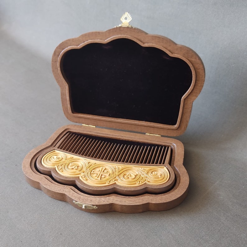 Puede incluir: Un peine de madera con tallas intrincadas en una caja de madera decorativa con forro de terciopelo. La caja tiene forma de corona y tiene un cierre de metal dorado.
