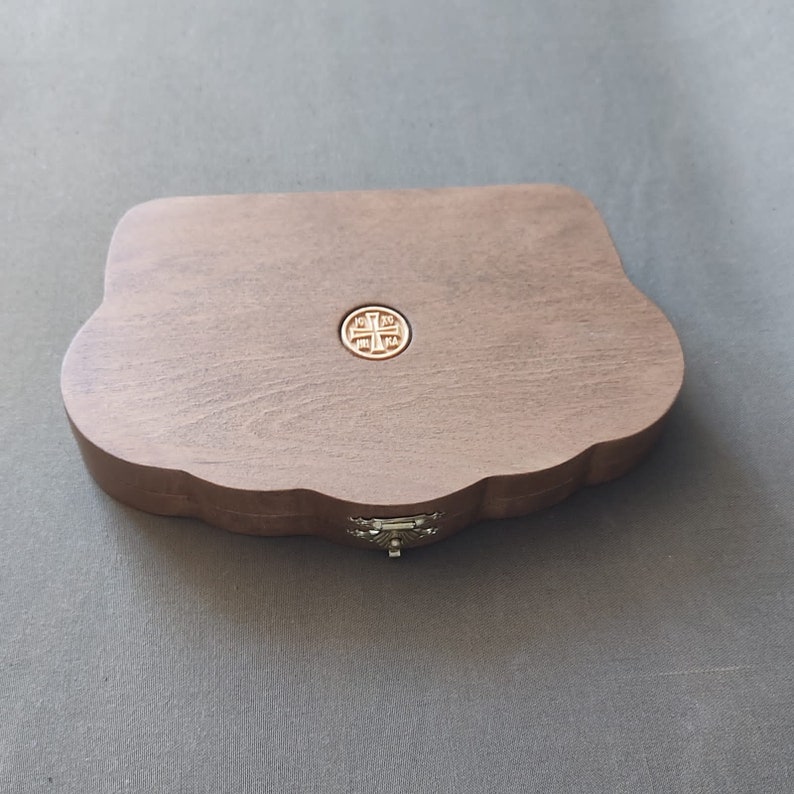 Puede incluir: Una caja de madera con un dise&ntilde;o decorativo y ornamentado. La caja tiene una tapa con bisagras y un cierre de metal. La parte superior de la caja presenta un dise&ntilde;o circular grabado con una cruz.
