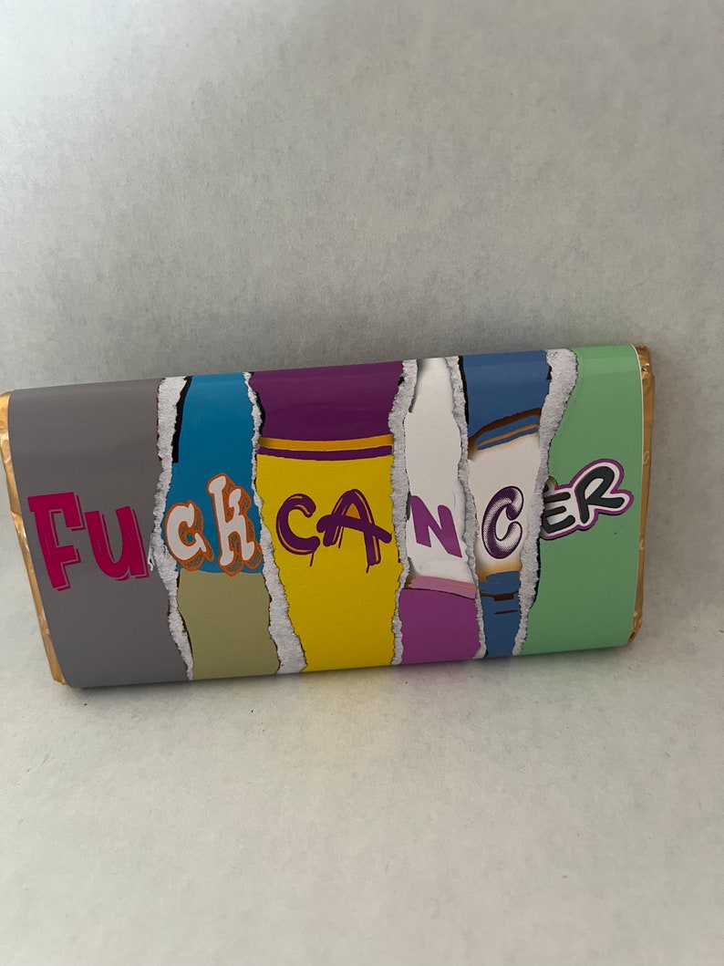 Puede incluir: Envoltorio de barra de chocolate con las palabras "Fuck Cancer" en un dise&ntilde;o colorido de papel rasgado. El envoltorio tiene un borde dorado y un fondo gris.