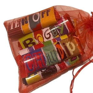 May include: A red organza gift bag containing several candy rolls. The wrappers display words such as "Off", "Bogey", and "Chilli Dip" in diverse fonts and colours. The bag is secured with a red ribbon.