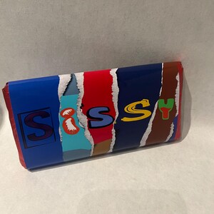 May include: A blue, red, brown, and yellow candy bar wrapper with the word "Sissy" printed on it in a colorful, stylized font.