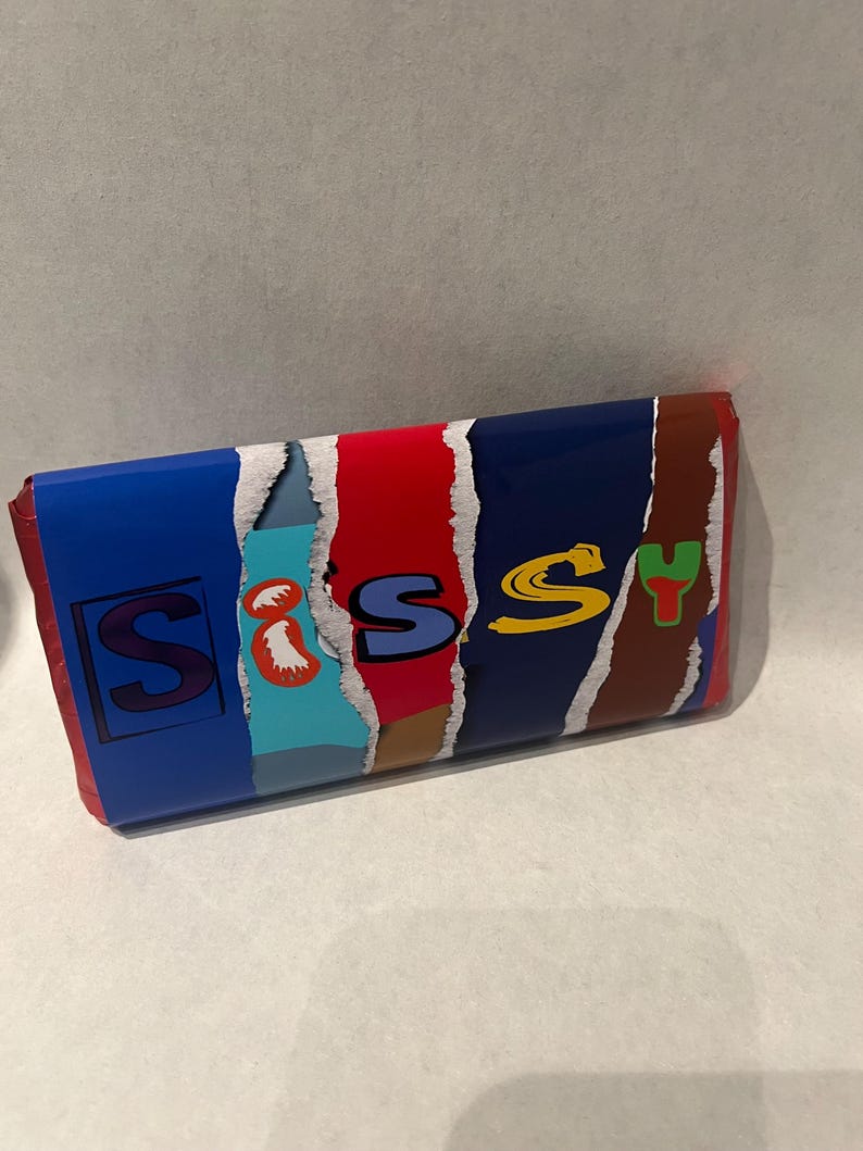 May include: A blue, red, brown, and yellow candy bar wrapper with the word "Sissy" printed on it in a colorful, stylized font.